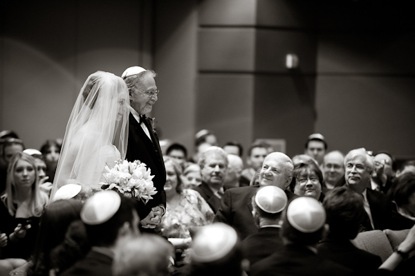 side shot -black and white photo- bride being walked down the aisle by father wearing a yamika -photo by Houston based wedding photographer Adam Nyholt